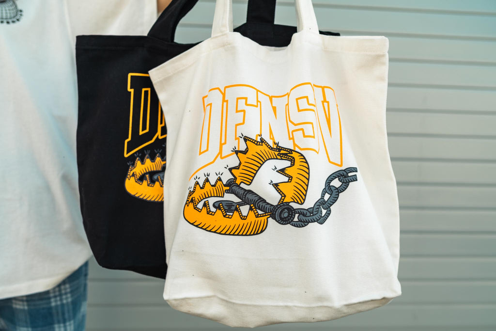 Canvas Tote bag comes in Black or Cream with Streetwear brand logo graphic design screen printed on front side modeled by male model and female model 
